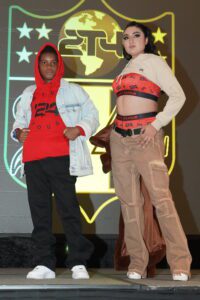 Two people standing on a stage wearing clothing.