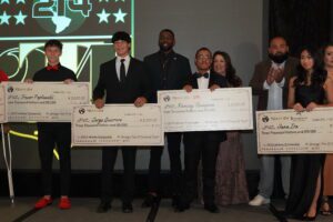 A group of people holding large cheques in front of a projector.