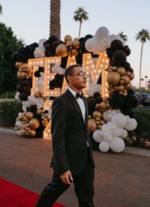 A man in a suit and tie standing next to balloons.