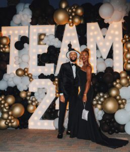 A man and woman posing in front of balloons.