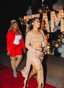 Two women walking on a red carpet in front of balloons.