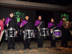 A group of men in purple shirts playing drums.