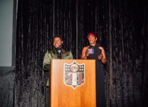 Two people standing at a podium in front of a shield.