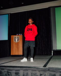 A man in red jacket standing on stage.