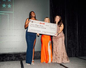 Three women holding a giant check in front of them.