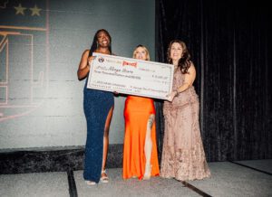 Three women holding a giant check in front of them.