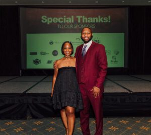 A man and woman posing for a picture in front of a screen.