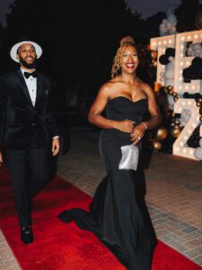 A man and woman in black dress on red carpet.