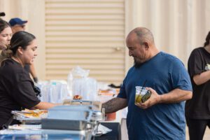 Two men standing at a table with food.