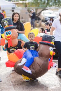 A child sitting on an inflatable turkey next to two turkeys.