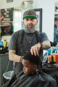 A man with a beard and glasses is cutting the hair of a boy.