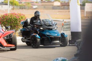 A man riding on the back of a blue three wheeled motorcycle.