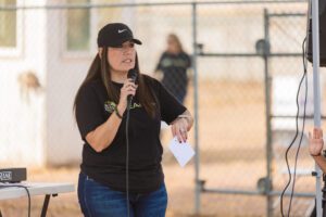 A woman in black shirt holding microphone near fence.