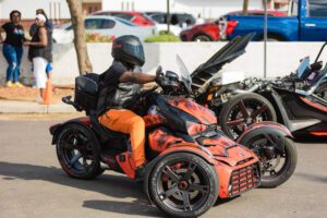 A person on an orange and black three wheeled motorcycle.