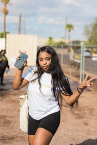 A woman holding up two fingers while standing on the street.