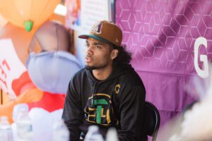 A man sitting in front of balloons wearing a hat.