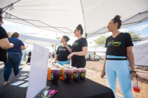 Three women standing around a table with drinks.