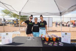 Three women standing under a tent with drinks.