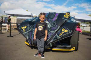 A young boy standing next to an upside down car.