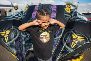 A young boy standing in front of a car.