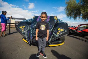 A young boy standing in front of a car.