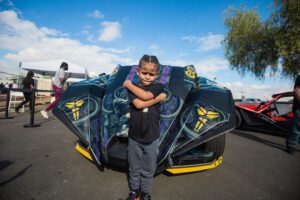 A young boy standing next to a car with a hood painted on it.