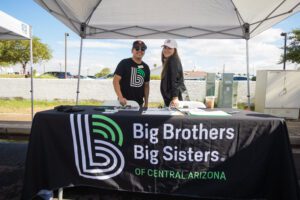 Two people standing under a tent with big brothers big sisters of central arizona logo.