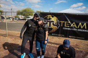 Two people posing for a picture in front of a t 4 team banner.