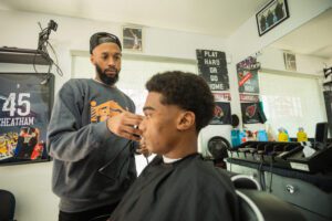 A barber cutting another man 's hair in his shop.