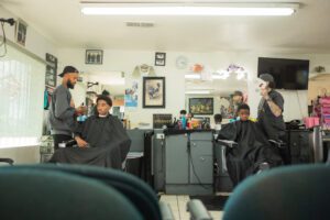 A group of people sitting in chairs at a barber shop.