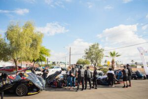 A group of people standing around motorcycles parked in the street.