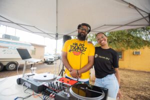 Two people standing next to a dj booth.