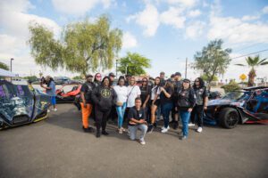 A group of people standing in front of some cars.