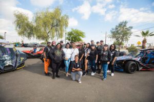 A group of people standing in front of some cars.