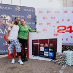 A man and woman posing for the camera in front of a giant tv.