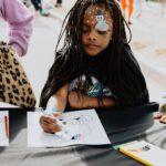 A young girl with dreadlocks is drawing.