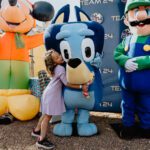 A little girl kissing the nose of a large character.