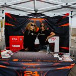 Two women posing for a picture in front of an orange and black tent.