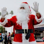 A man in santa clause costume waving at the camera.