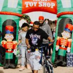 A man riding a bike in front of inflatable toy soldiers.