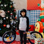 A boy standing in front of christmas tree and presents.