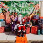 A man in santa suit sitting on the ground with two women.