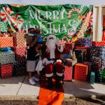 A person in santa suit standing next to a bunch of presents.