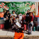 A group of people standing around santa clause.