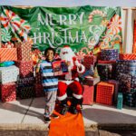 A boy standing next to santa clause in front of some presents.