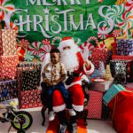 A child sitting on santa 's lap in front of a christmas sign.