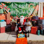 A child posing with santa claus in front of many presents.