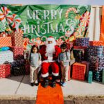 A man in santa suit sitting on the ground with two children.