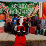 A man in santa claus costume sitting on top of a red sleigh.