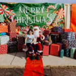 A person sitting on santa 's lap in front of many presents.